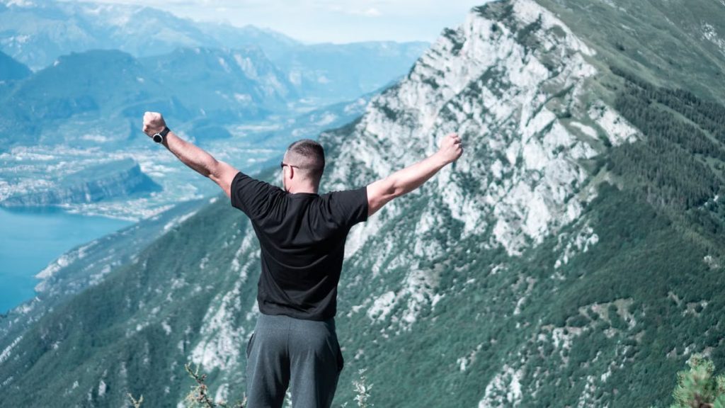 Man standing with arms raised in celebration overlooking a breathtaking mountain landscape.